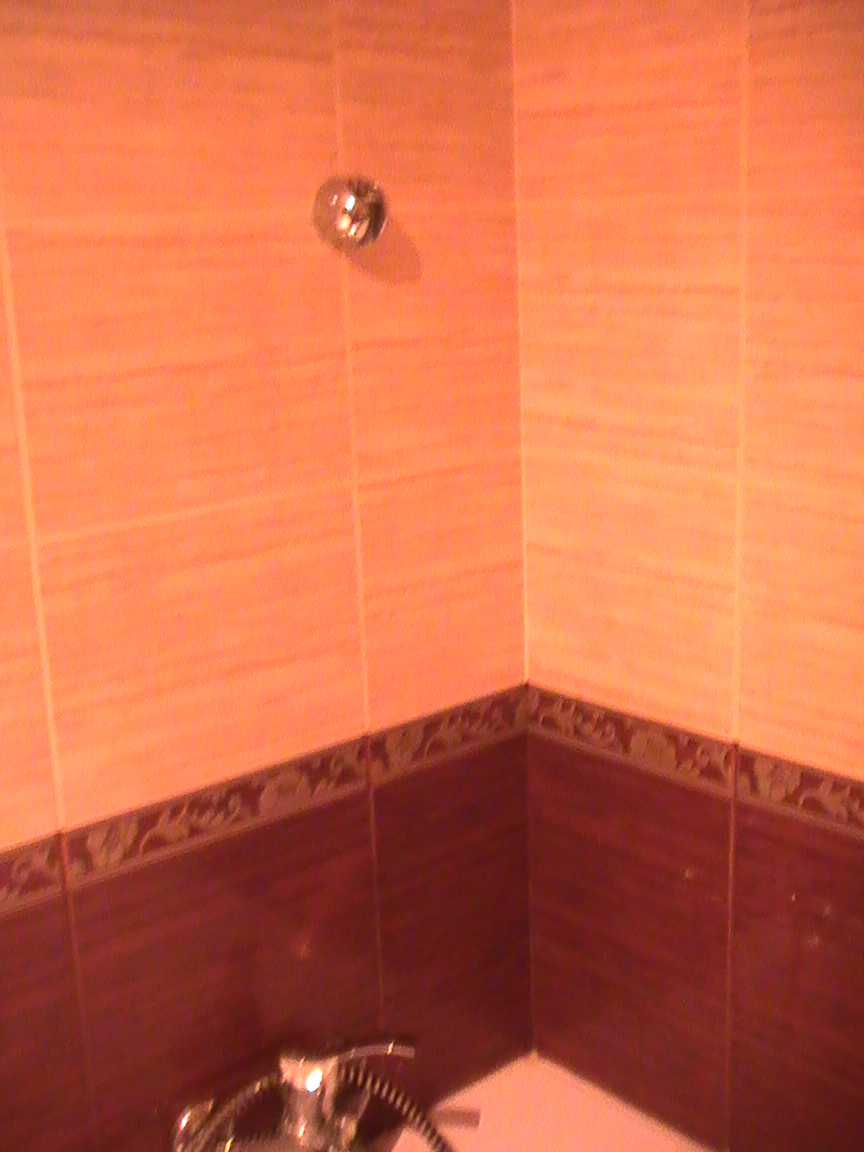 Wykończona łazienka z brązowymi i pomarańczowymi płytkami, widoczny prysznic i bateria.